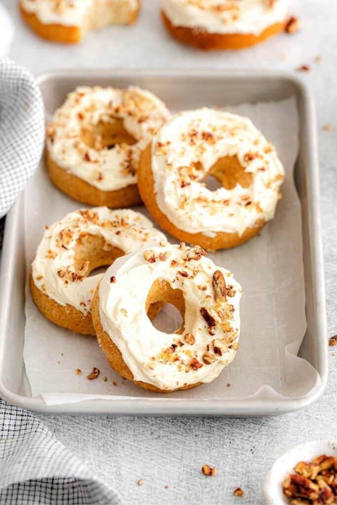 Four maple donuts served on a parchment paper-lined baking tray.