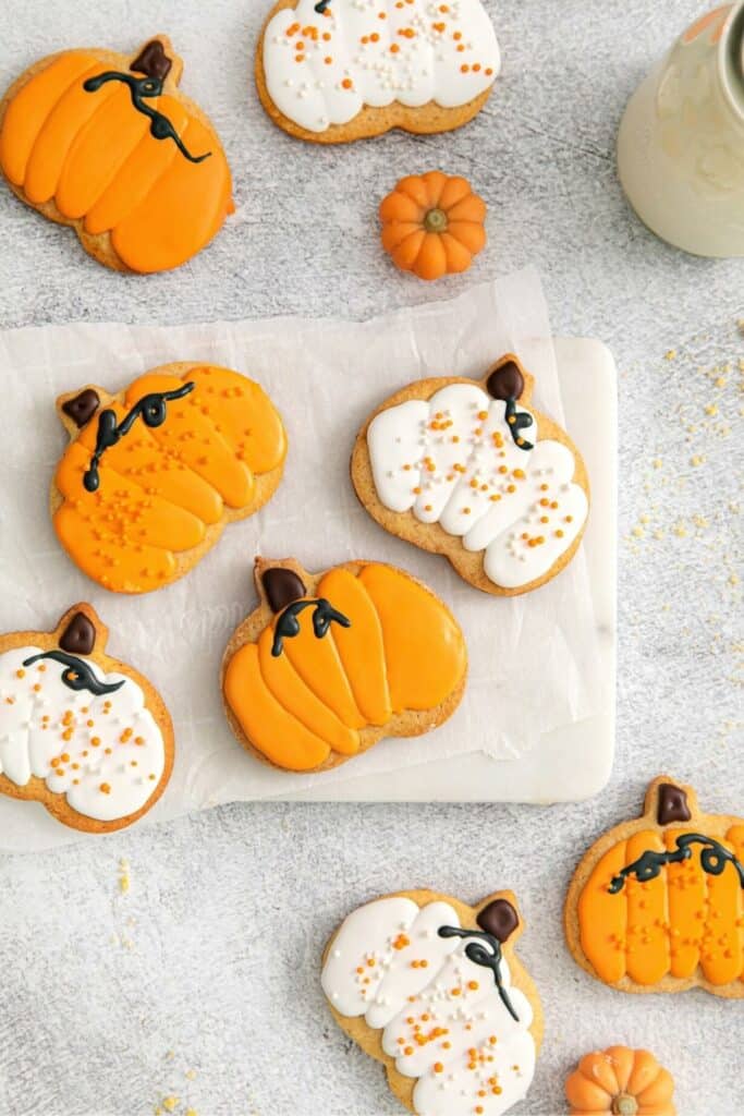 Pumpkin shaped sugar cookies on a countertop with a glass bottle of milk.