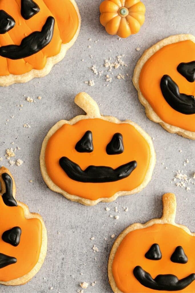 Five Halloween Jack-o'-lantern sugar cookies with orange frosting and black icing details.