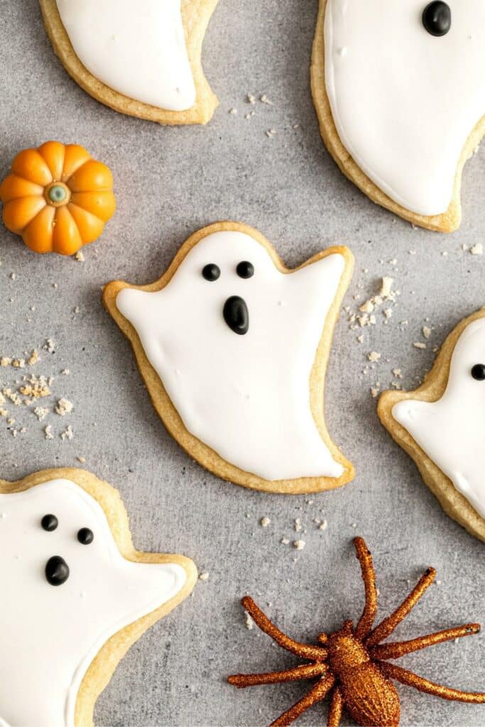 Halloween Ghost cookies on a countertop with a sparkly orange spider and mini pumpkin.