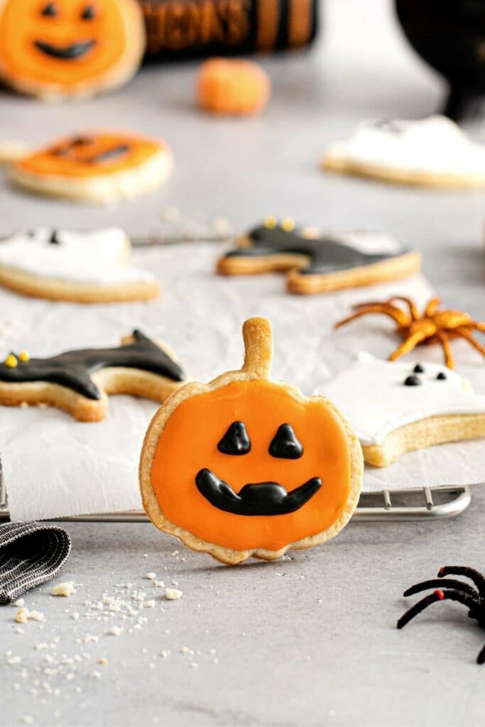 One Jack-o'-lantern cookie propped up against a wire rack where other iced Halloween cookies are drying.
