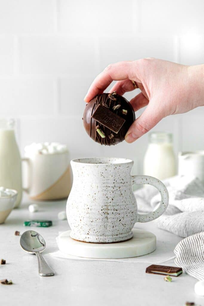 Hand holding a hot cocoa bomb over a mug getting read to put it in.