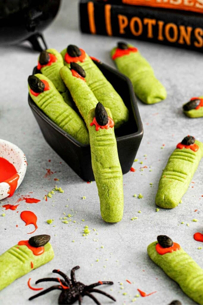Witch finger cookies in a black ceramic casket serving dish on a dessert table.