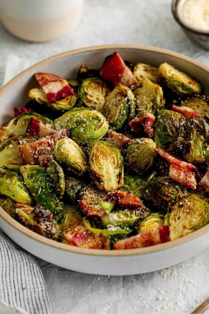 Brussels sprouts in a serving bowl garnished with crispy bacon and parmesan cheese.