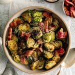 Air fryer Brussels sprouts with bacon garnished with grated Parmesan in a serving bowl with spoon.