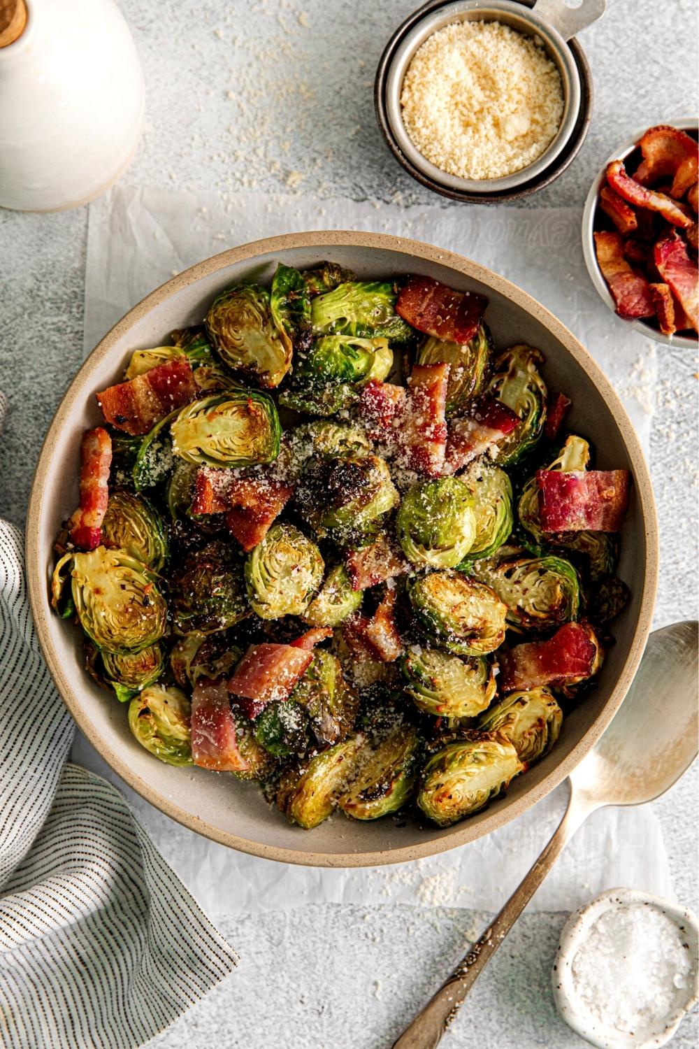 Air fryer Brussels sprouts with bacon garnished with grated Parmesan in a serving bowl with spoon.