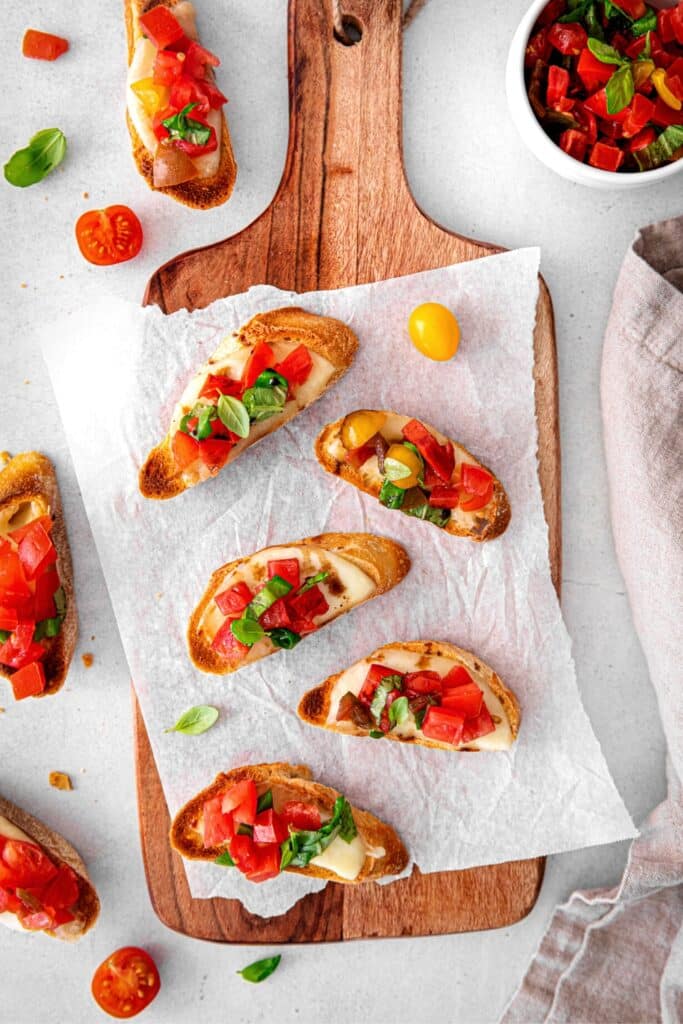 Bruschetta with cheese on a serving board with an extra bowl of marinated tomatoes.