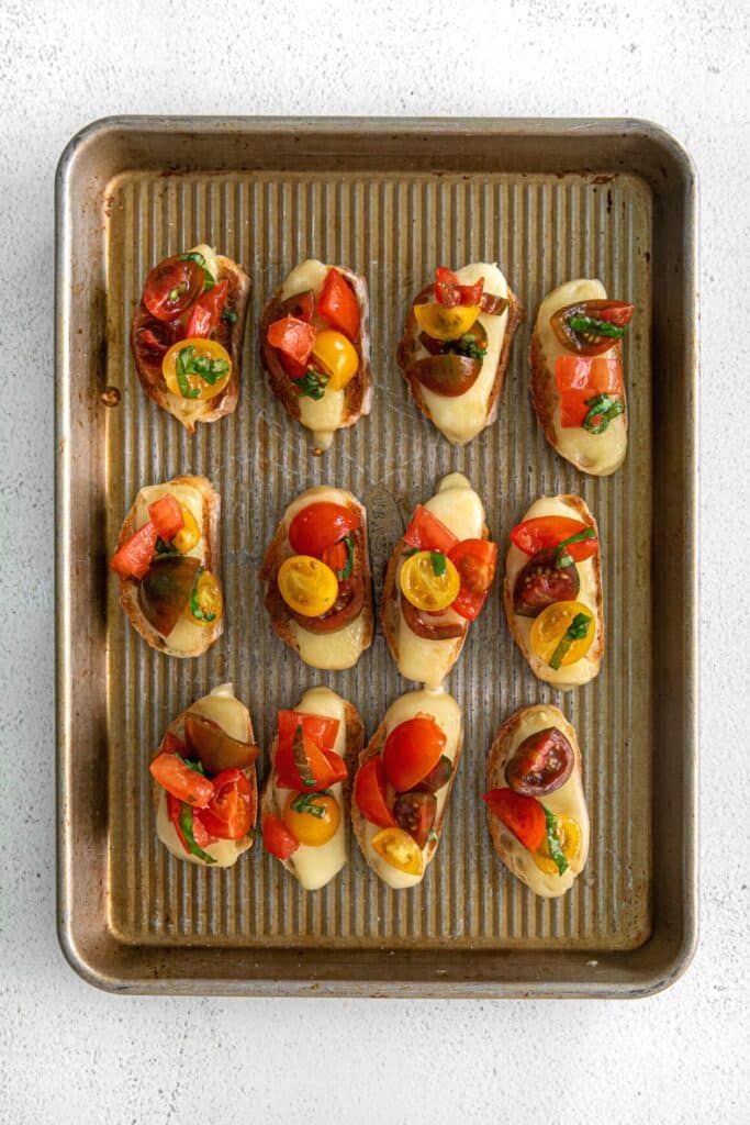 Twelve pieces of bruschetta with mozzarella on a baking tray.