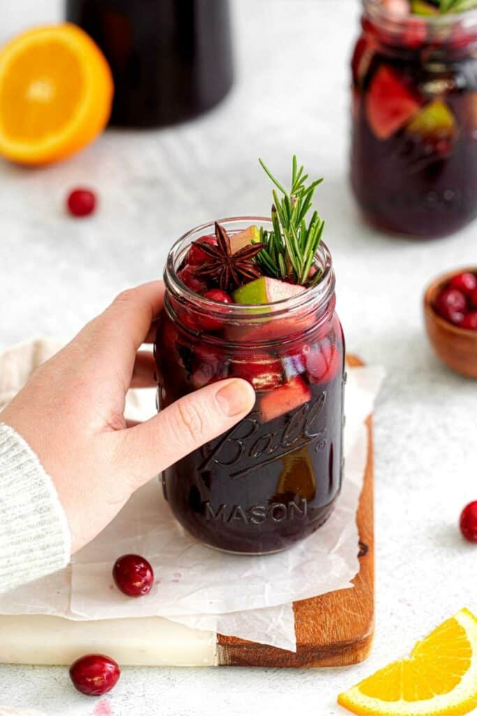 A hand reaching for a mason jar of Christmas sangria set on a wooden/marble board.