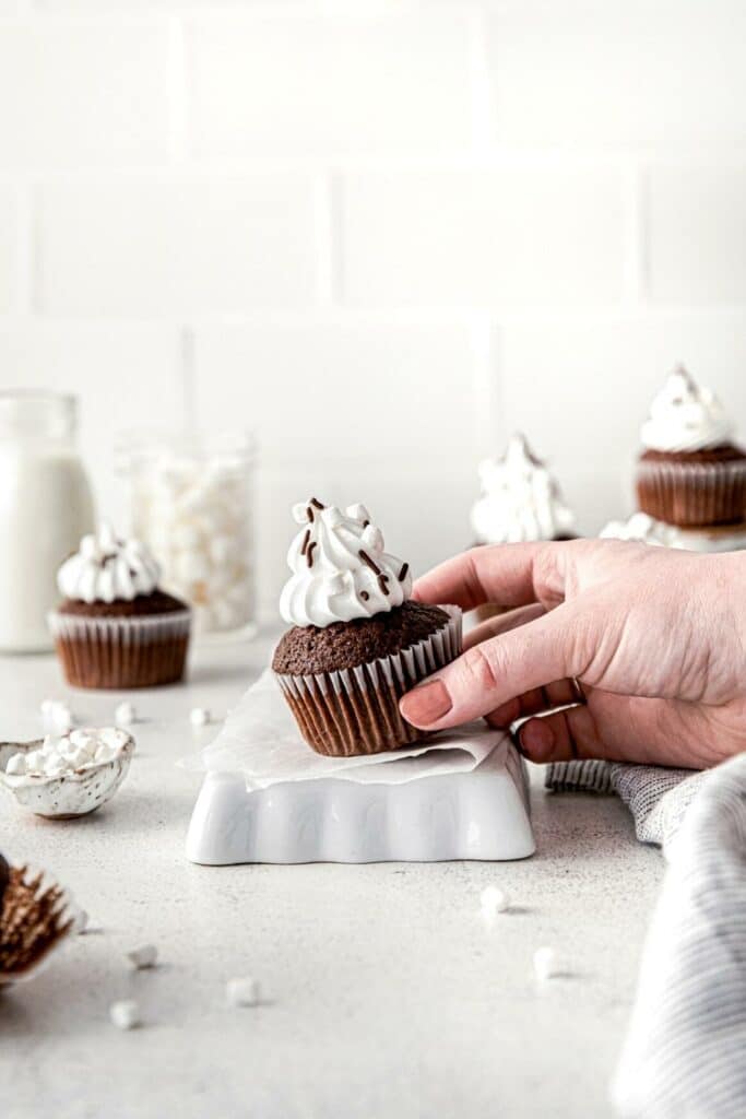 Hand lifting a hot chocolate cupcake from a dessert table.