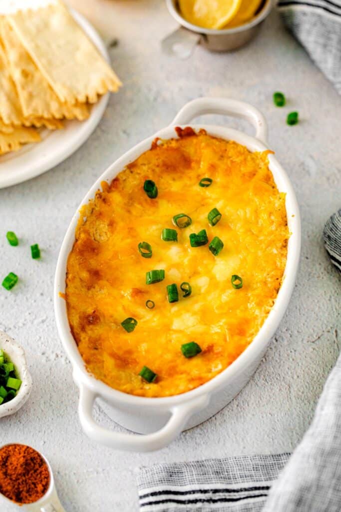 Hot crab dip in a white oval baker served served with rustic crackers.
