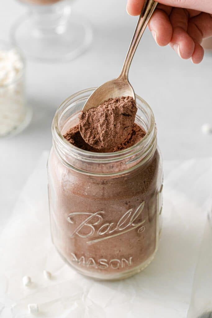 Homemade hot chocolate mix being scooped from a mason jar with a spoon.