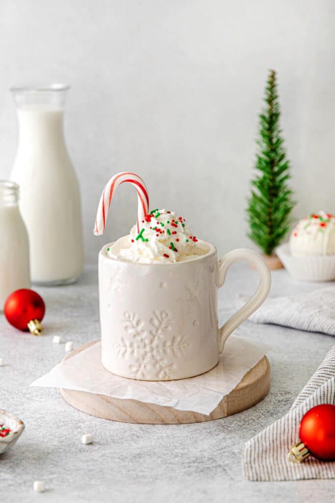 Mug of Christmas hot chocolate with whipped cream, Christmas sprinkles and a candy cane.
