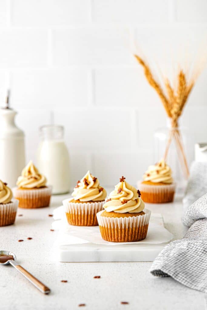 Five gingerbread cupcakes with salted caramel buttercream frosting on a serving table with milk.