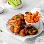 Dry rub chicken wings served on a plate with carrot and celery sticks.