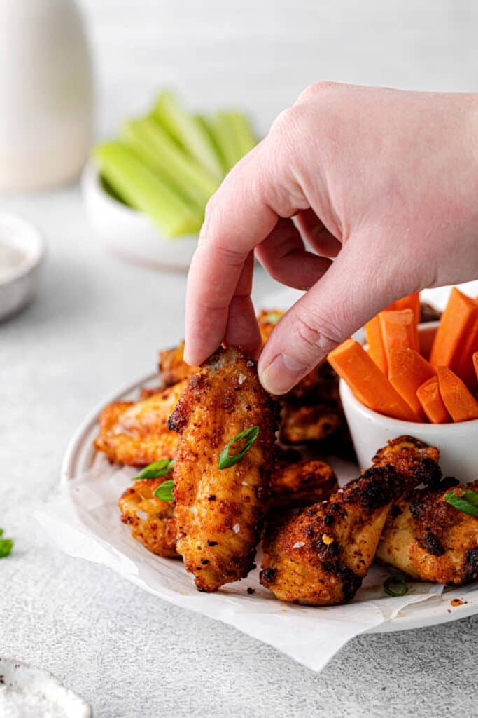 Hand lifting a dry rub chicken wing from an appetizer plate.