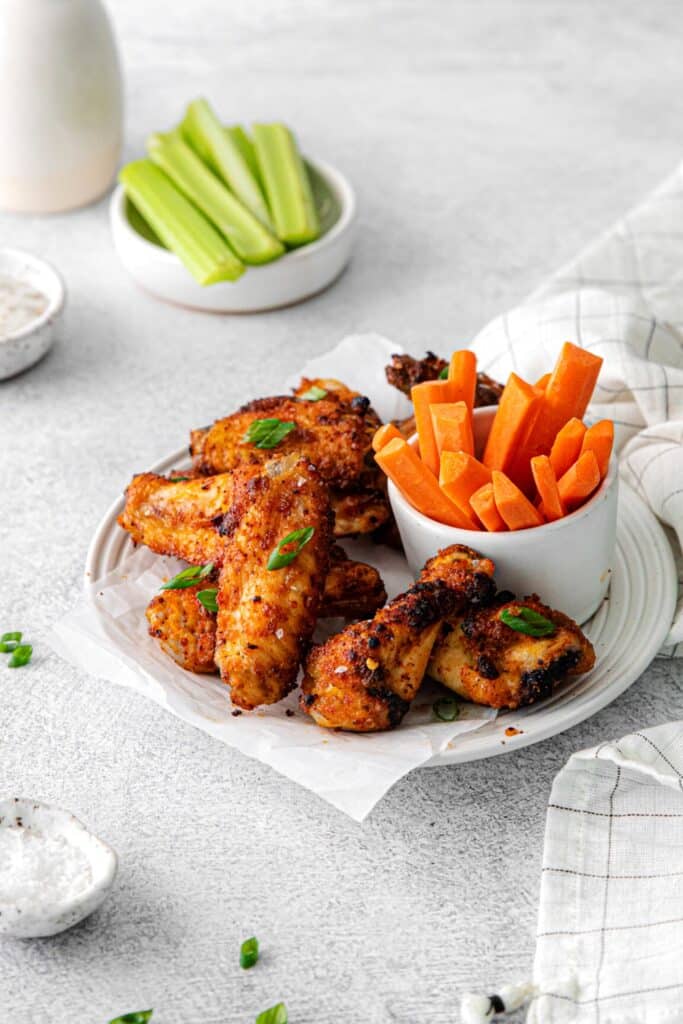 Dry rub chicken wings served on a plate with carrot and celery sticks.