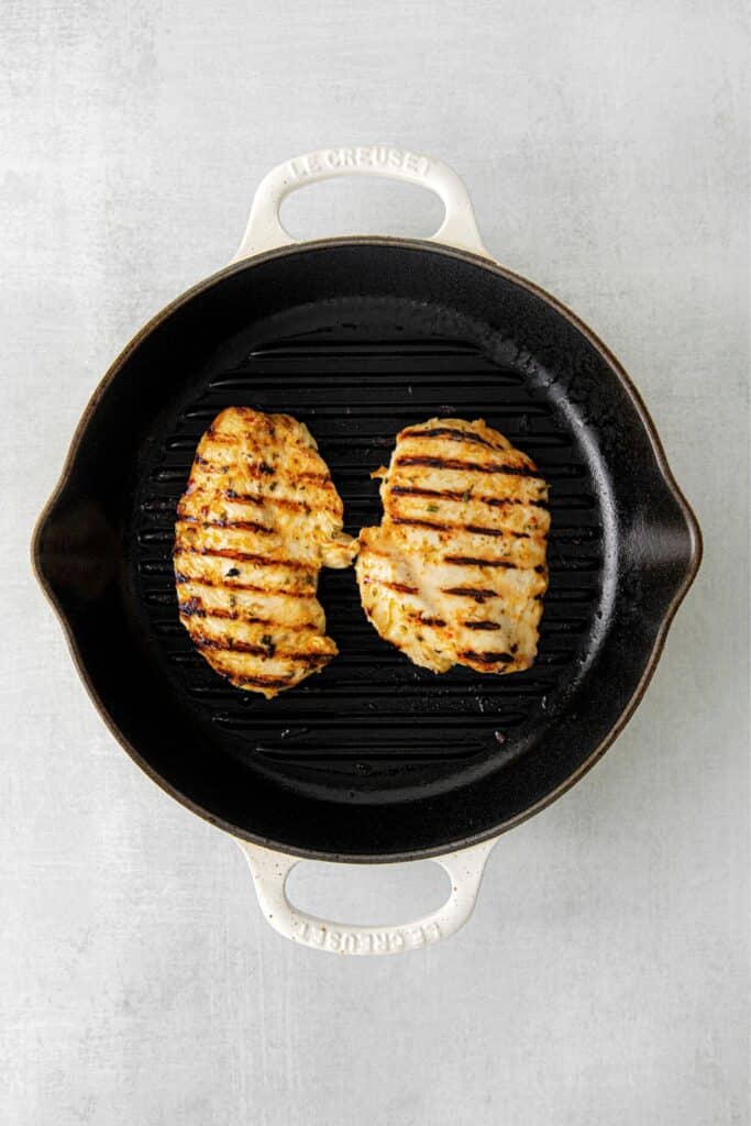 Two grilled chicken breasts in a Le Creuset grill pan.