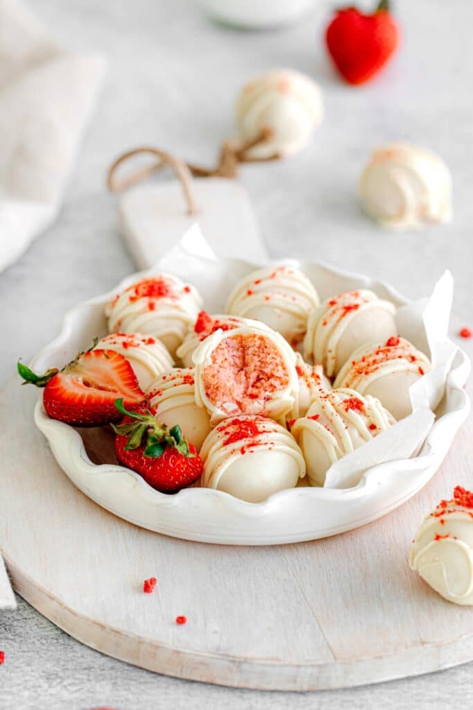 Strawberry cake truffles in a white fluted serving dish with fresh strawberries.