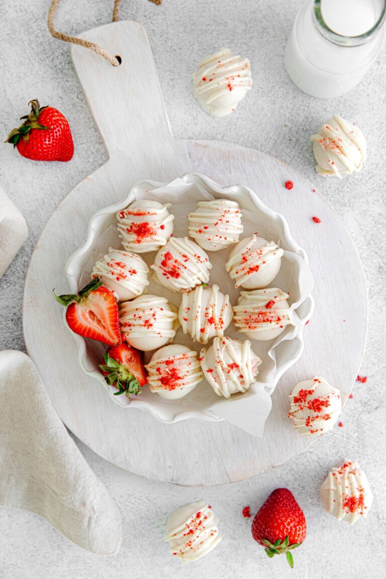 Batch of homemade cake truffles on a white wooden board with fresh strawberries and milk.