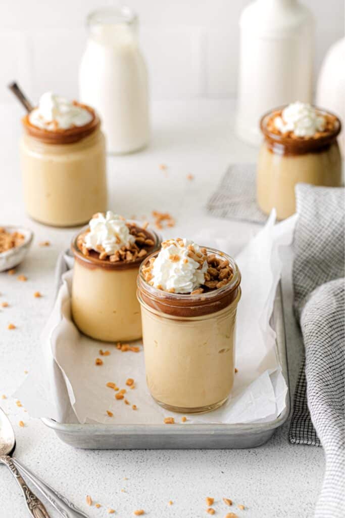 Four servings of butterscotch pudding topped with caramel sauce, whipped cream and chopped nuts.