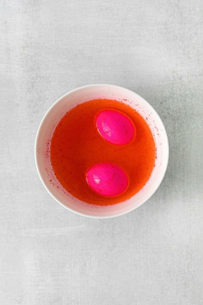 A small bowl with neon pink food dye and 2 Easter eggs.