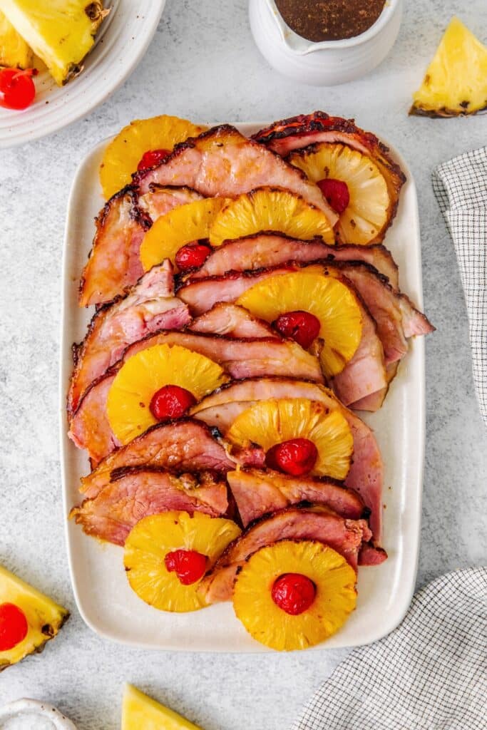 Spiral ham slices arranged on a platter with pineapple slices and maraschino cherries.