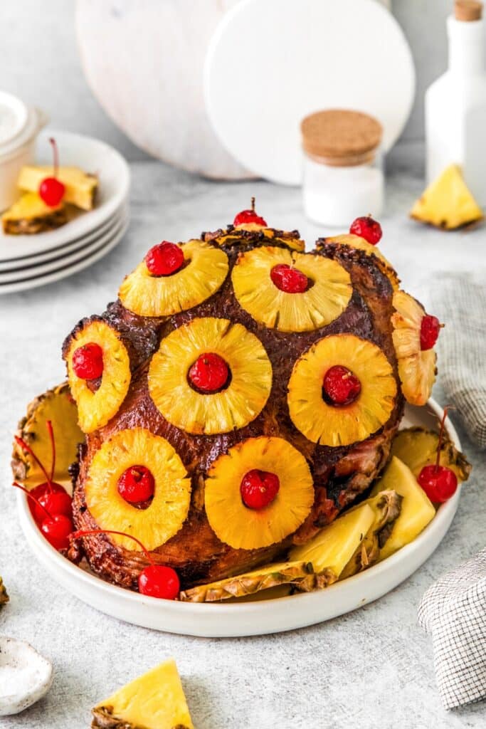 Stunning pineapple ham with brown sugar glaze on a platter next to a stack of plates.