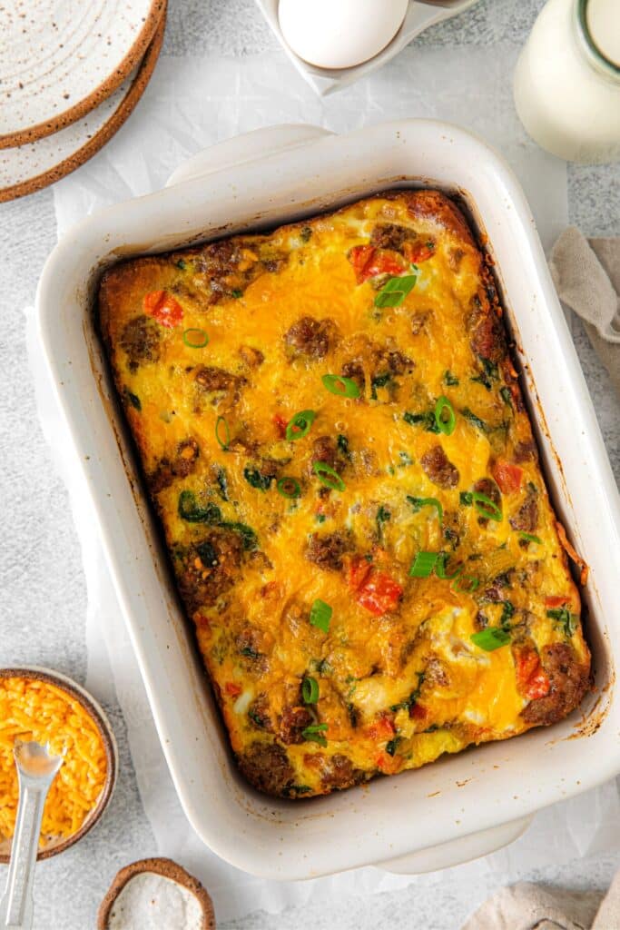 Sausage breakfast casserole in a baking dish next to a stack of plates.