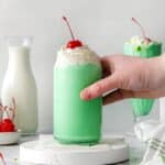 A glass of cool, refreshing shamrock shake on a white drink coaster with a hand about to lift up the glass.
