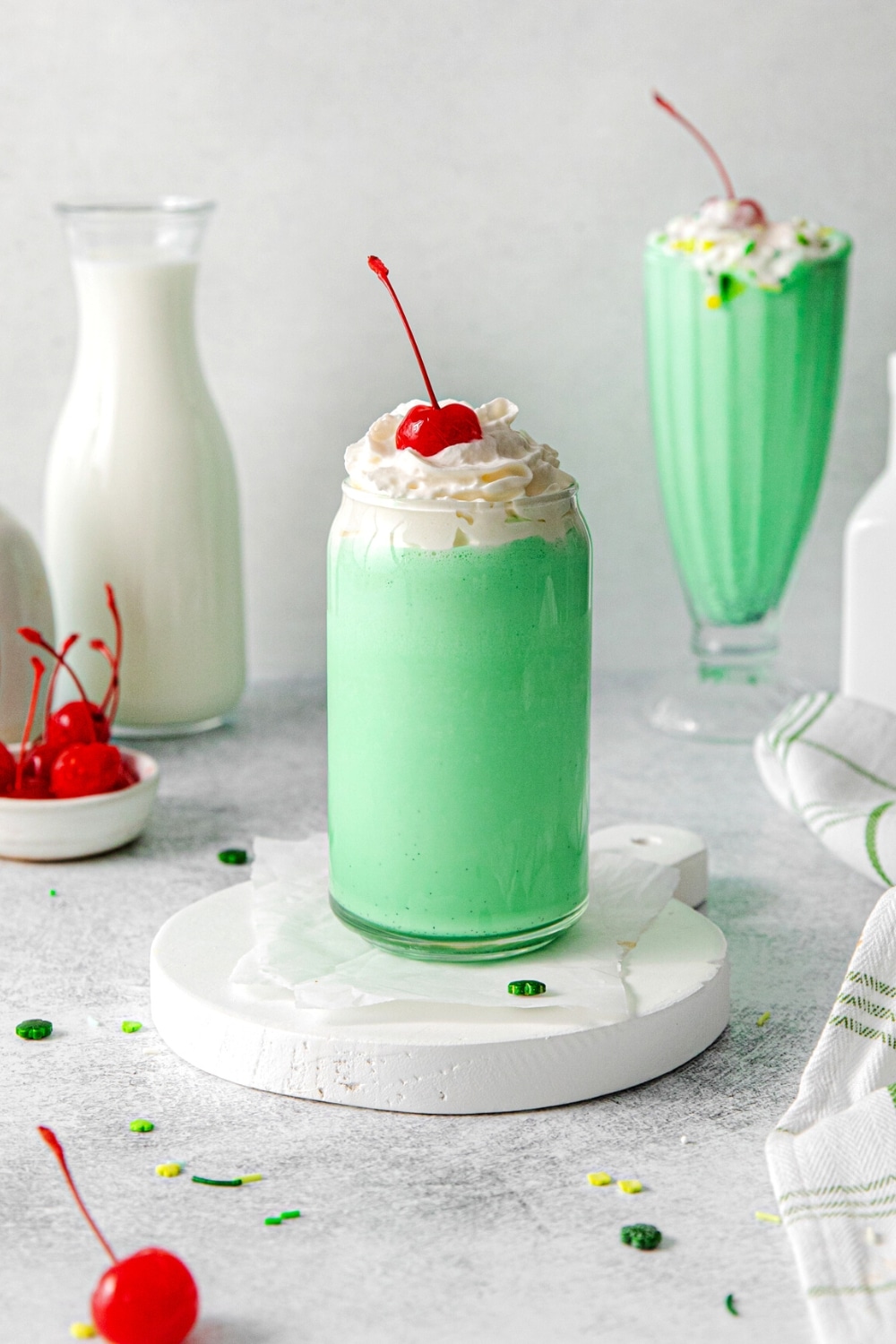 A copycat McDonald's shamrock shake garnished with whipped cream and maraschino cherry, with an additional shake in the background.