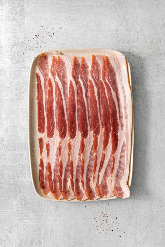 Uncooked bacon slices on a rectangle tray.
