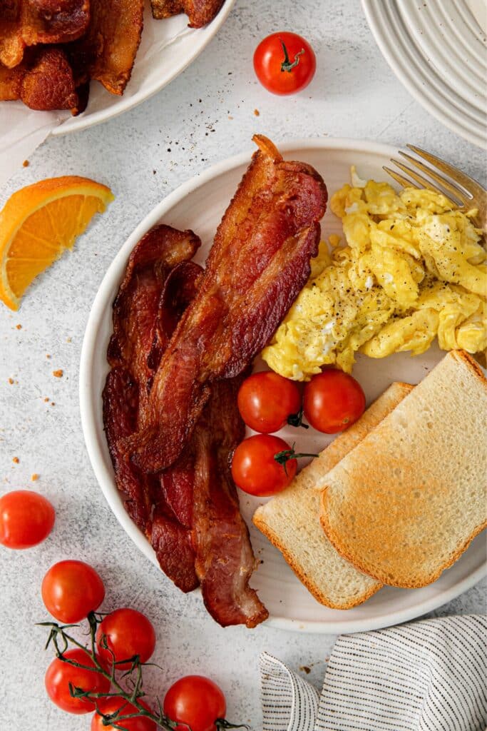A breakfast plate with bacon, scrambled eggs, toast and cherry tomatoes.