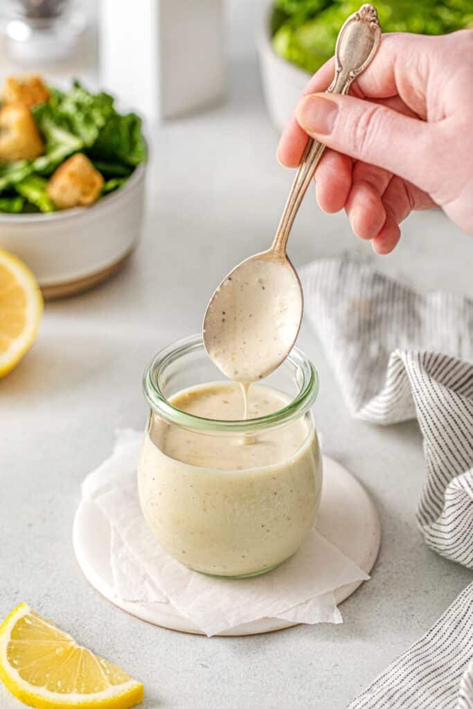 Creamy, healthy Caesar dressing dripping down from a spoon into a salad dressing jar.