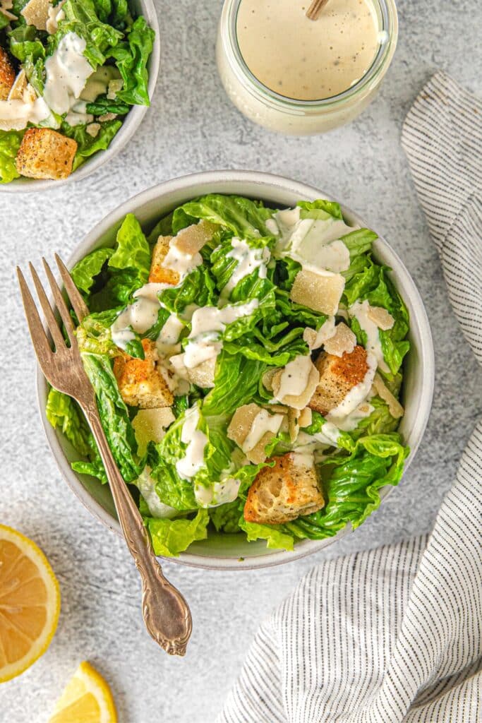 Serving of Caesar salad  with romaine lettuce, shaved parmesan, croutons and creamy Caesar dressing.