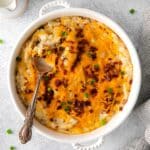 Loaded baked potato casserole in a round white baking dish with a silver serving spoon.