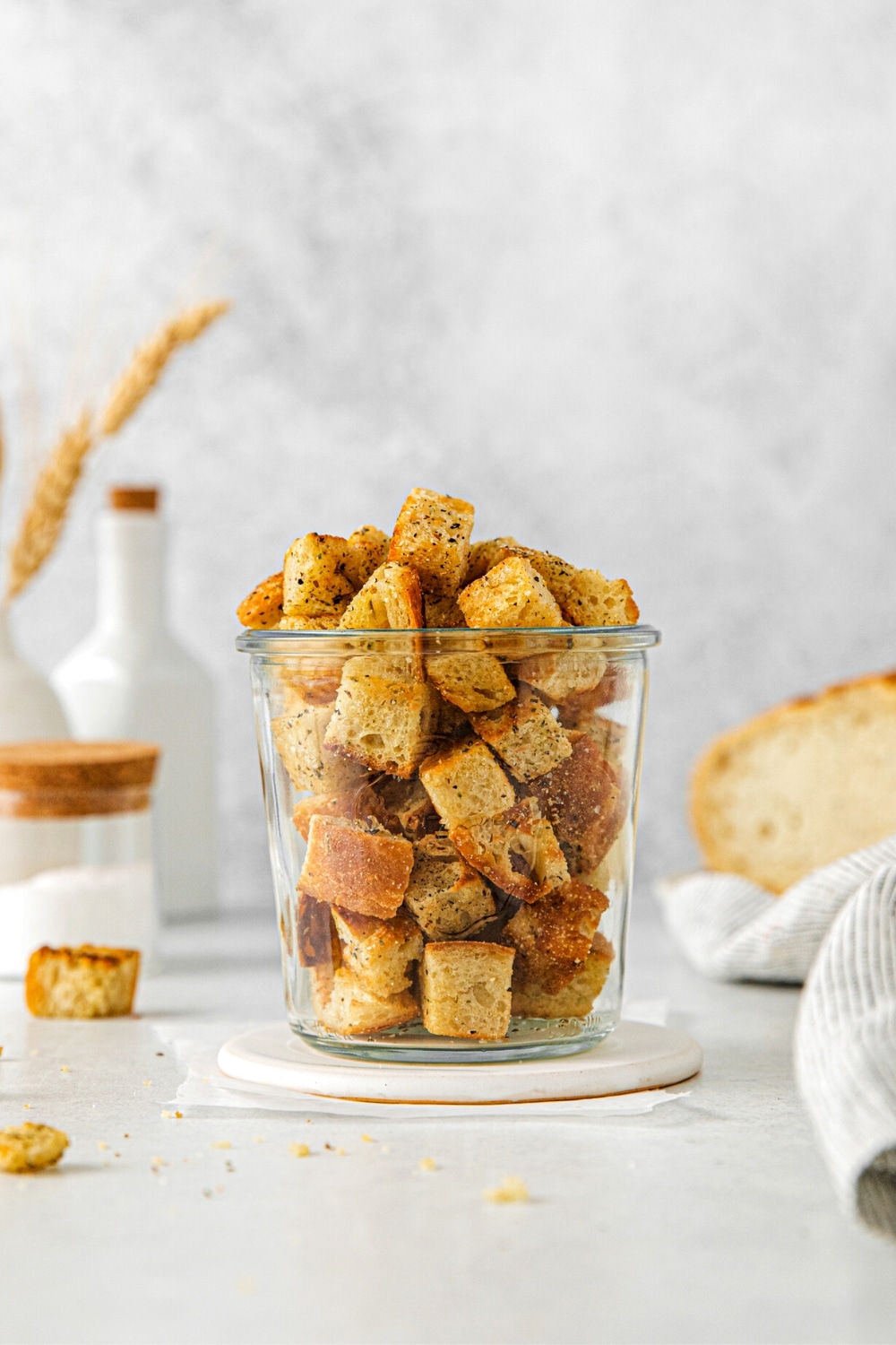 Mini sourdough croutons in a glass jar next to a loaf of sourdough bread.
