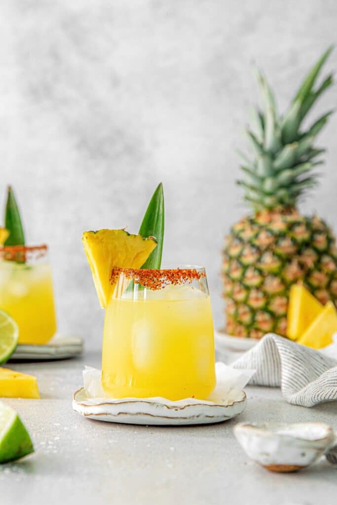 Pineapple Margarita in a Tajin-rimmed glass garnished with a fresh wedge of pineapple.
