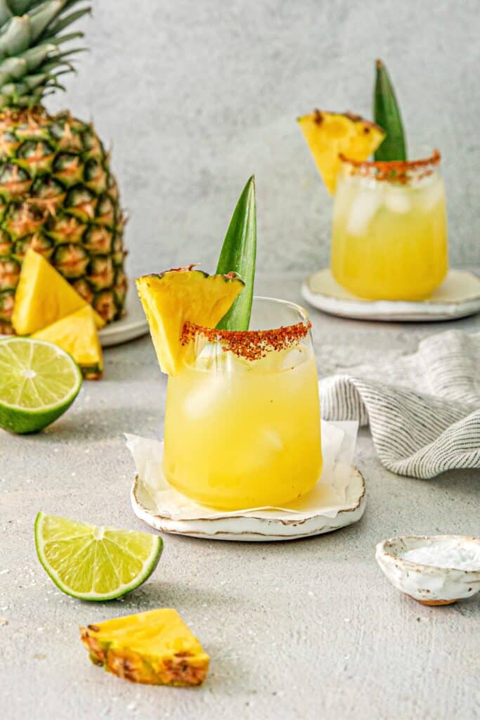 Pineapple Margaritas on a serving table with a fresh pineapple and limes.
