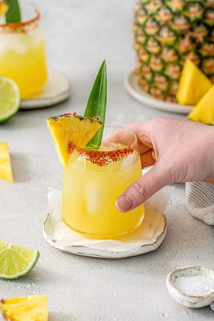 A hand lifting a pineapple Margarita up from a drink coaster.