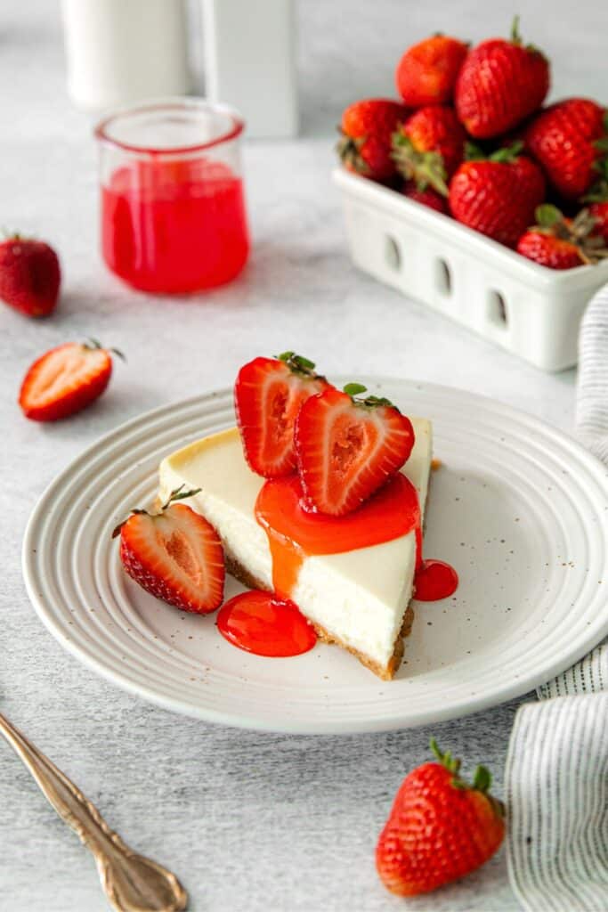 A slice of cheesecake with strawberry sauce drizzled on top, and a fresh strawberry garnish.