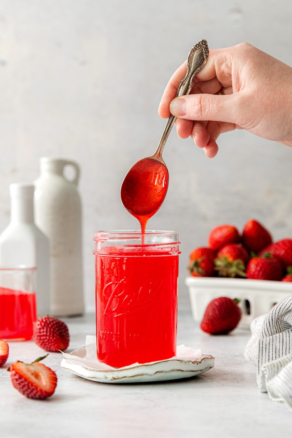 Homemade strawberry glaze dripping off a spoon into a mason jar next to fresh strawberries.