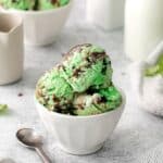Three rounded scoops of mint chocolate chip ice cream in a dessert cup with spoon.