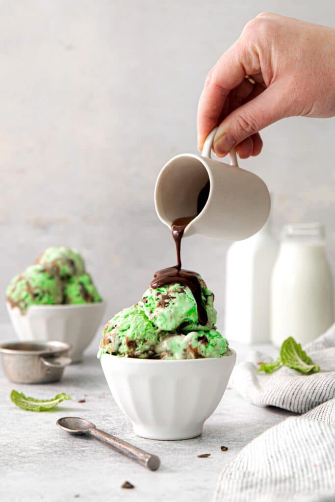 Hot fudge being poured over a serving of mint chocolate chip ice cream.