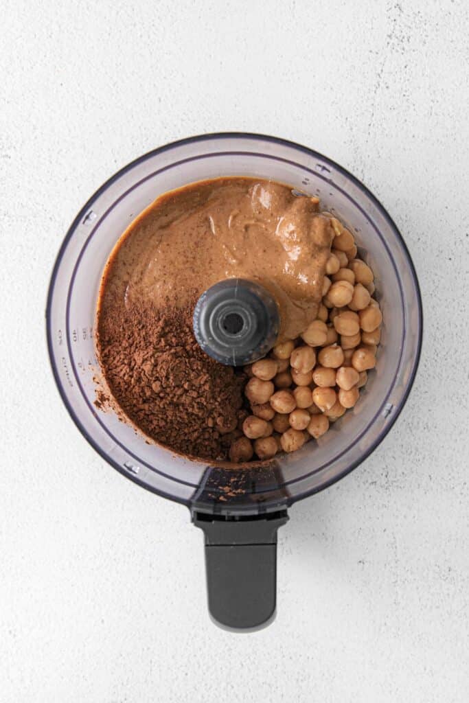 All the ingredients for chocolate hummus recipe added to the bowl of a food processor.