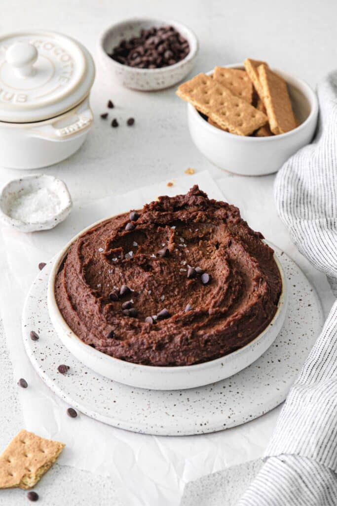 Dark chocolate hummus in a small bowl with flaky salt and chocolate chips. Served with graham crackers for dipping.