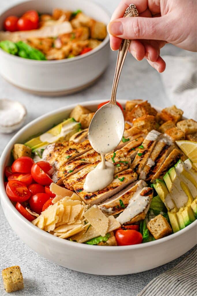 Drizzling Caesar salad dressing over a grilled chicken Caesar salad.
