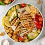 Grilled chicken Caesar salad topped with avocado, cherry tomatoes, shaved parmesan, croutons, dressing and lemon wedges.