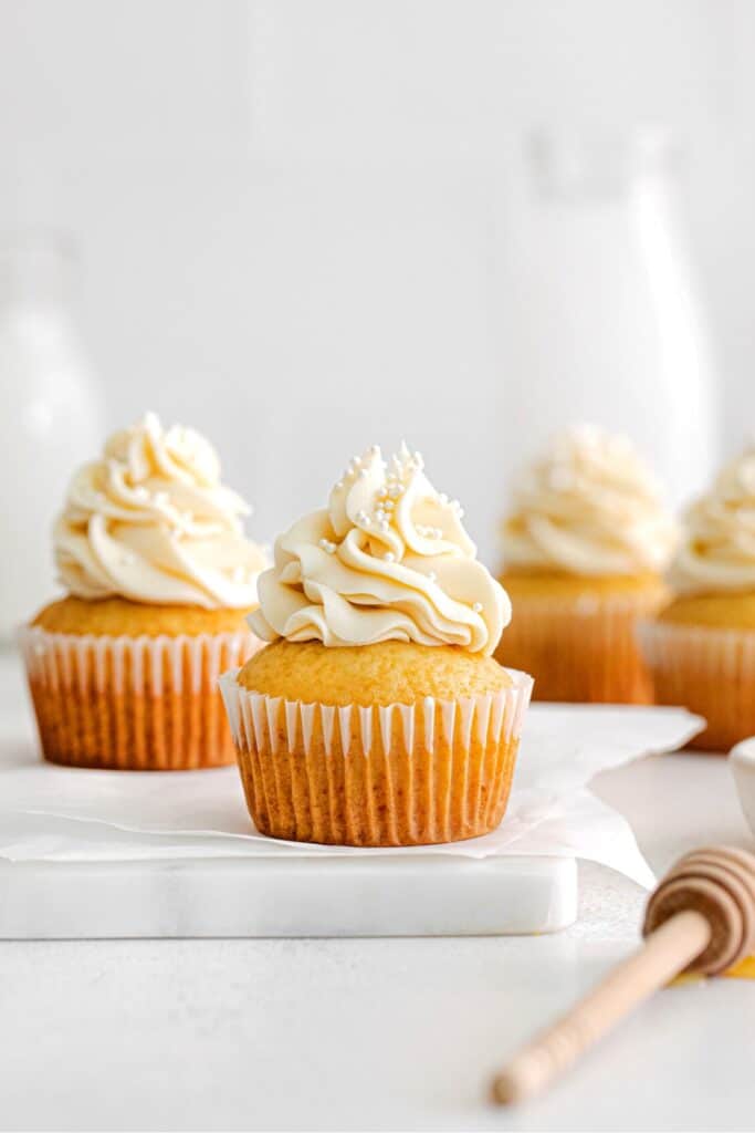 Honey cupcakes topped with honey buttercream frosting on a small marble serving board.