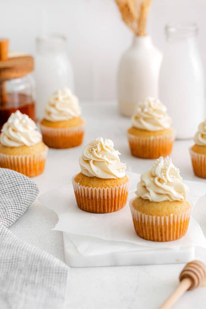 A batch of honey cupcakes on a dessert table with glass bottles of milk and honey jar.